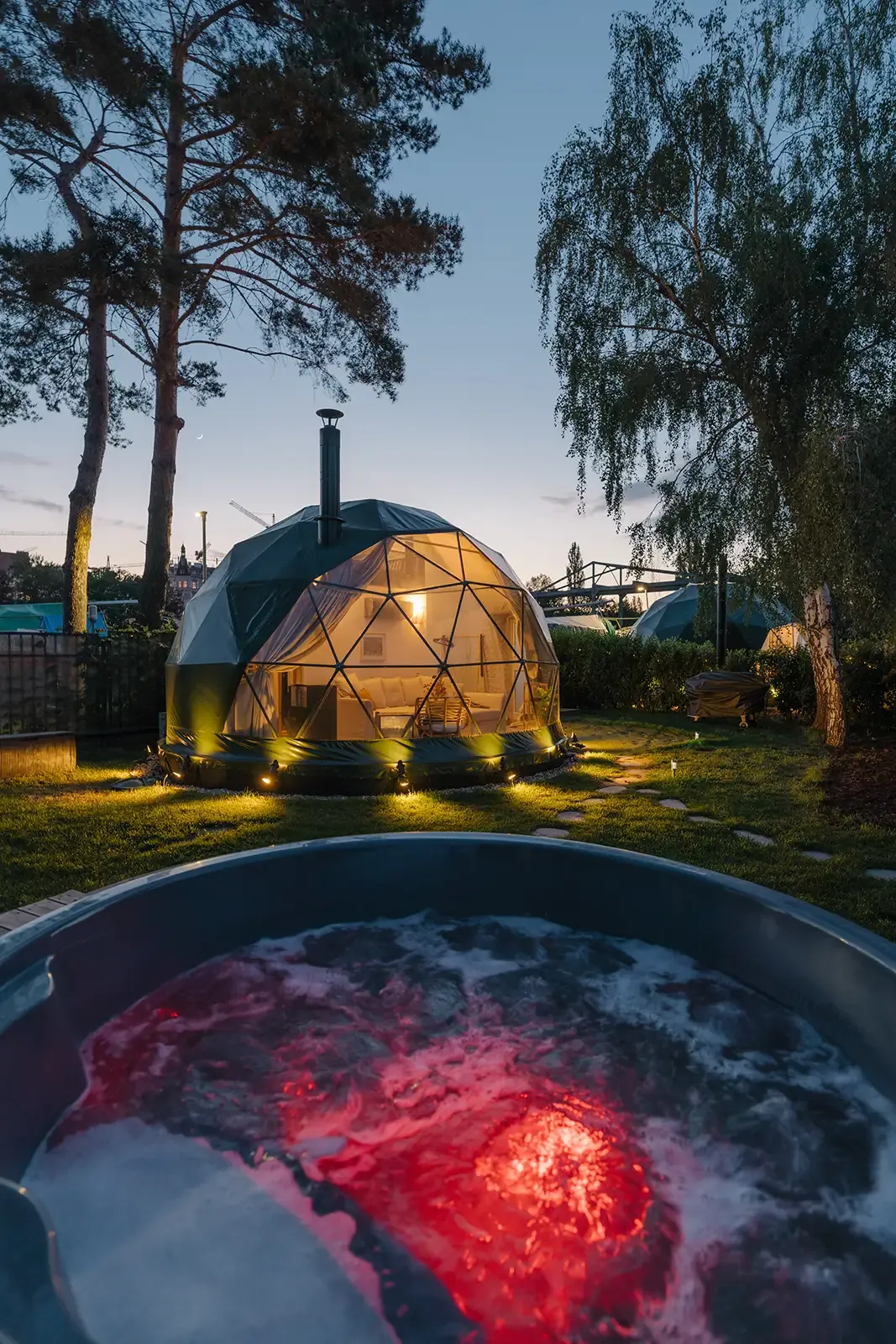 Geodesic dome lit at dusk with a wood-fired hot tub bubbling in the foreground