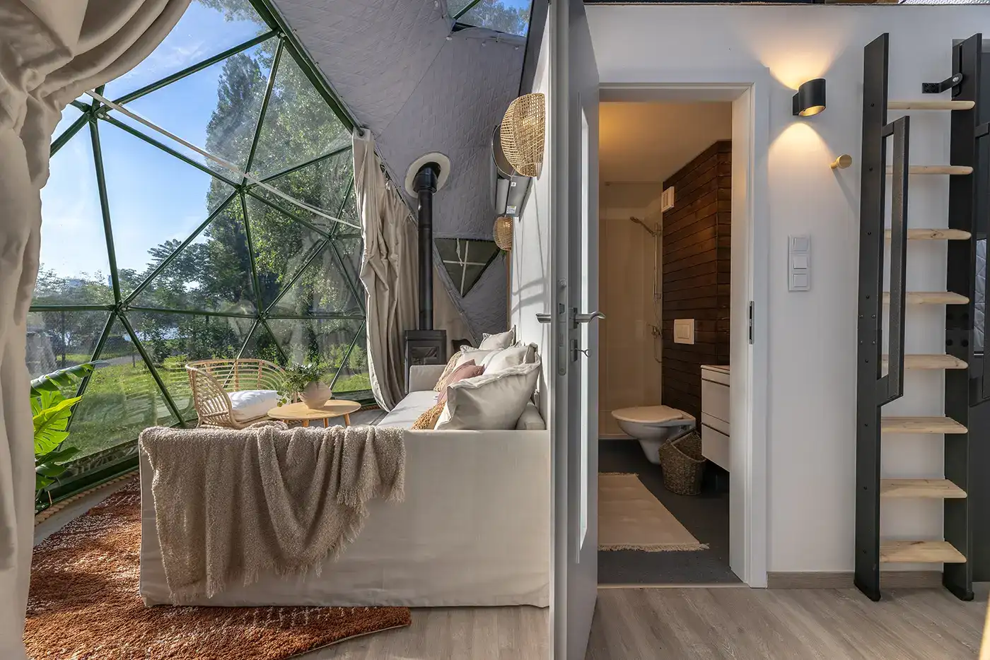 Dome interior: a linen sofa by the glass facade, with the bathroom and the stairs up to the bed beyond