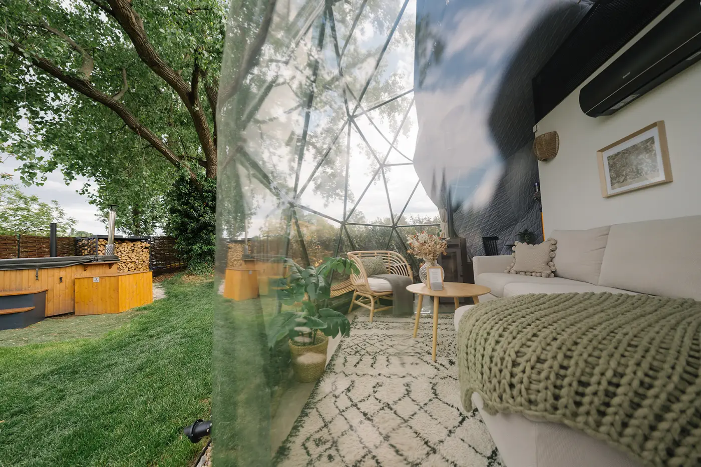 Dome interior with a bed and sofa looking out through the glass facade to the garden and wood-fired hot tub