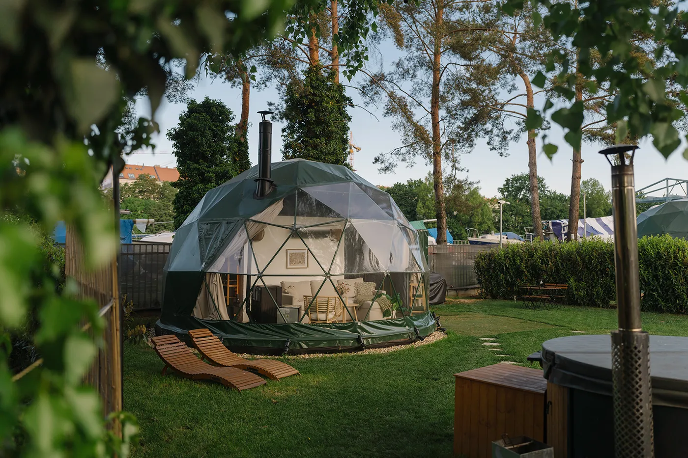 Geodesic dome at golden hour with a wooden lounger and a wood-fired hot tub in the garden